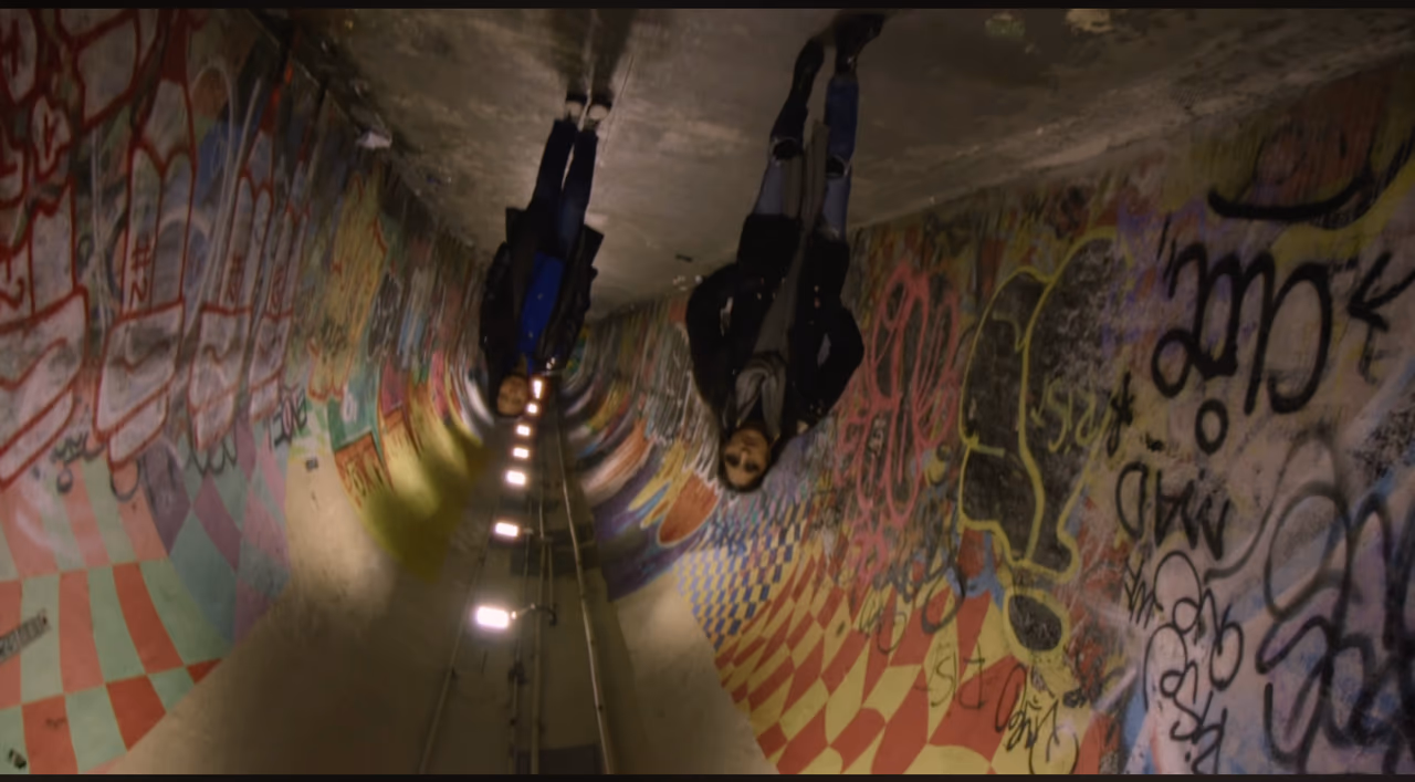 An upside-down shot of two people walking through a tunnel covered floor to ceiling in graffiti
