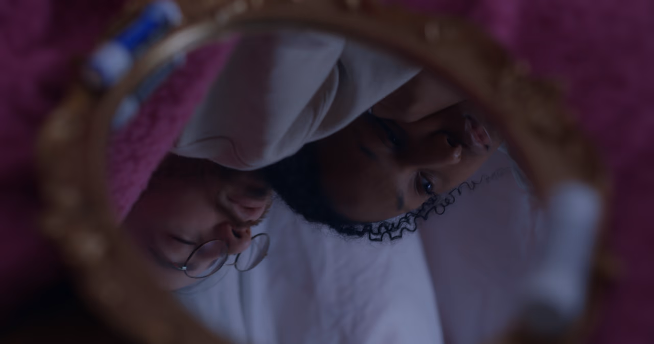 A couple's faces reflected upside down in a small round gold-framed mirror, his round glasses in the frame