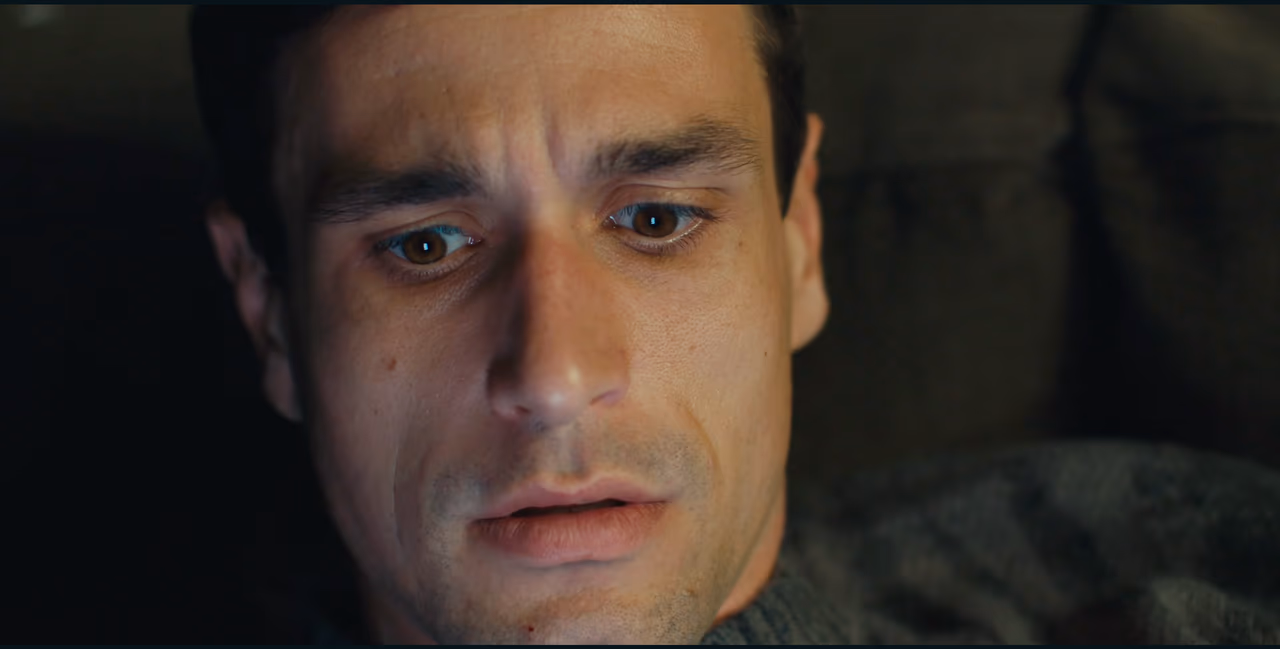 Close on a man's face, eyes wet and lowered, looking at something just below the frame