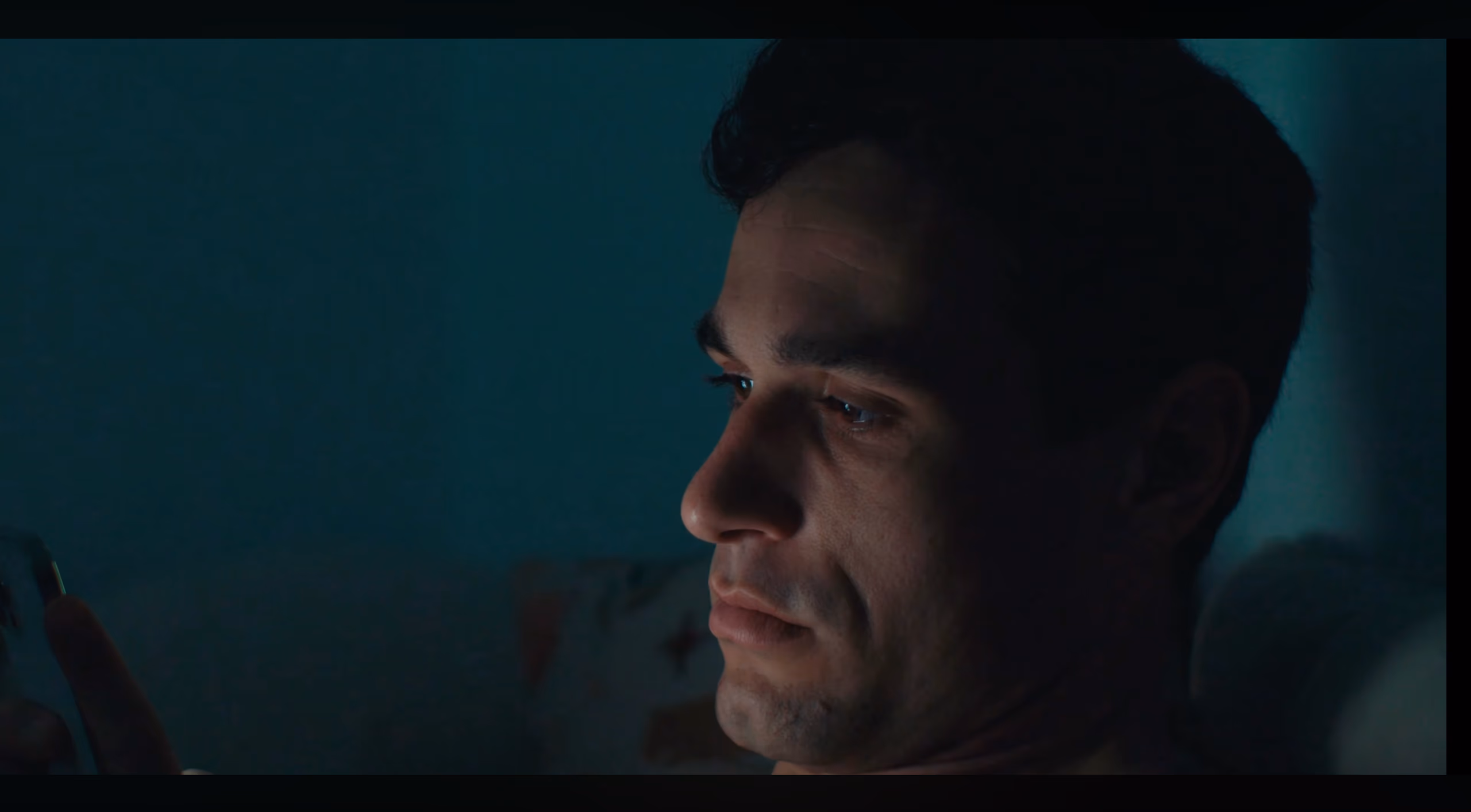 A man's face lit blue by the phone in his hand, in a dark teal room